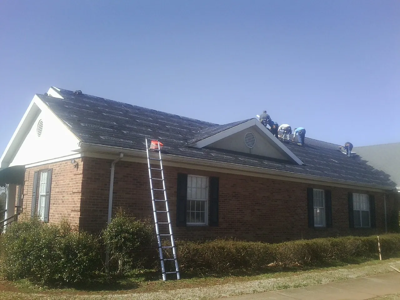 Crew tearing shingles off a brick ranch roof with a ladder set — Metal Roof Repair work by our crew in Botkins