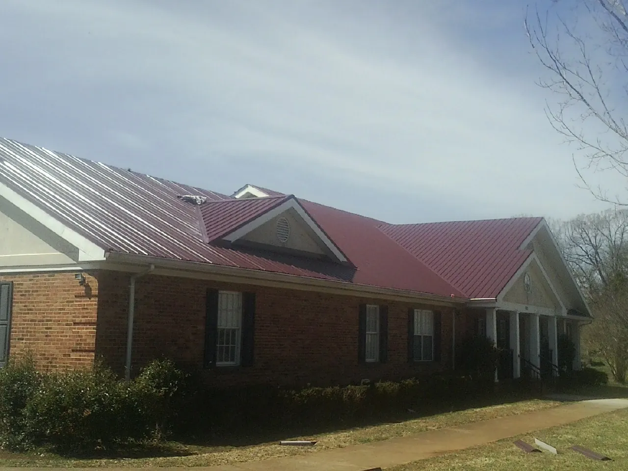 Red metal roof with gabled entries on a long brick building, from a Hail Damage Roof Repair job in Botkins