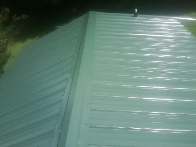 New green metal panels meeting at the ridge of a roof — Flat Roof Repair work by our crew in Botkins