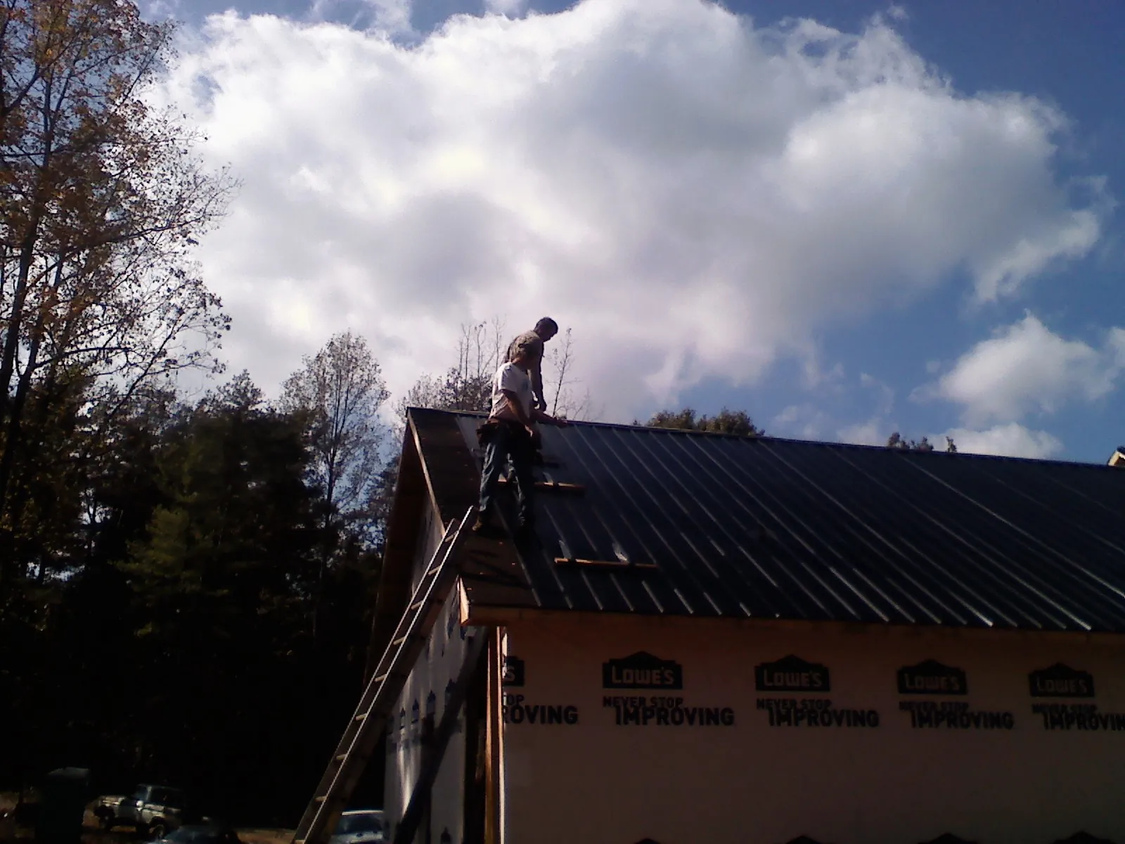 Roofer fastening dark metal panels high against a cloudy sky, from a Roof Inspection job in Botkins