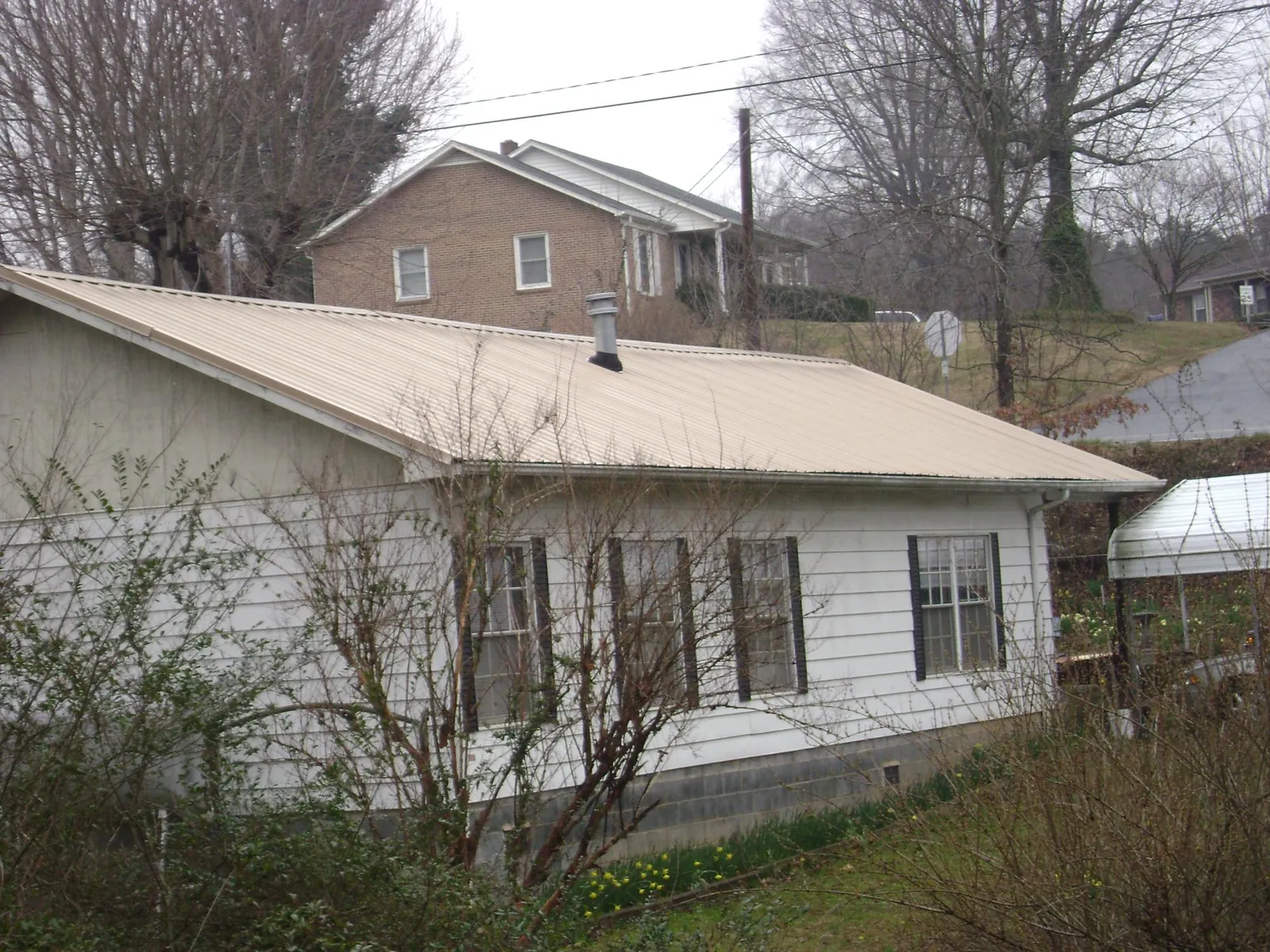 Tan metal roof on a white sided house set into a hillside — Commercial Roofing by Roofing Brothers in Botkins